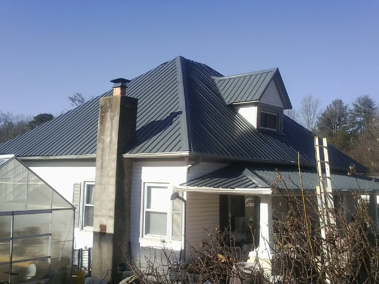 Dark blue standing seam metal roof on a white farmhouse with dormer — Slate & Tile Roof Repair by Roofing Brothers in West College Corner