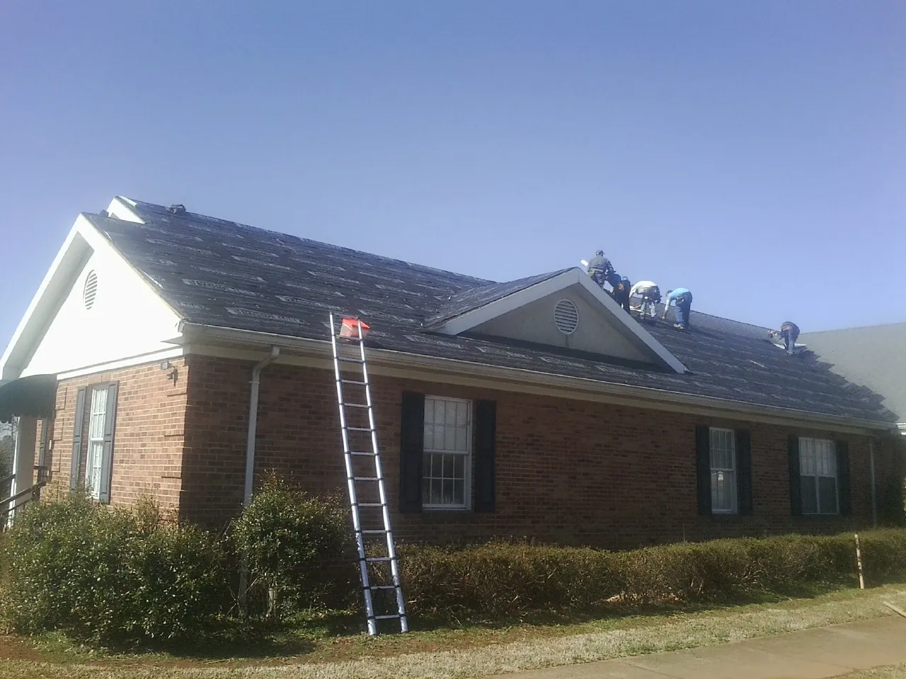 Crew tearing shingles off a brick ranch roof with a ladder set — Emergency Roof Repair work by our crew in West College Corner