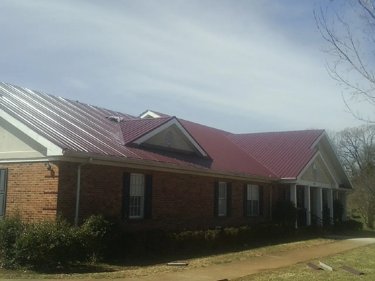 Red metal roof with gabled entries on a long brick building, from a Hail Damage Roof Repair job in West College Corner