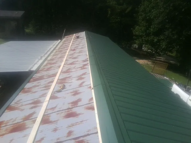Old rusted panels beside newly installed green metal roofing — Wind Damage Roof Repair by Roofing Brothers in West College Corner