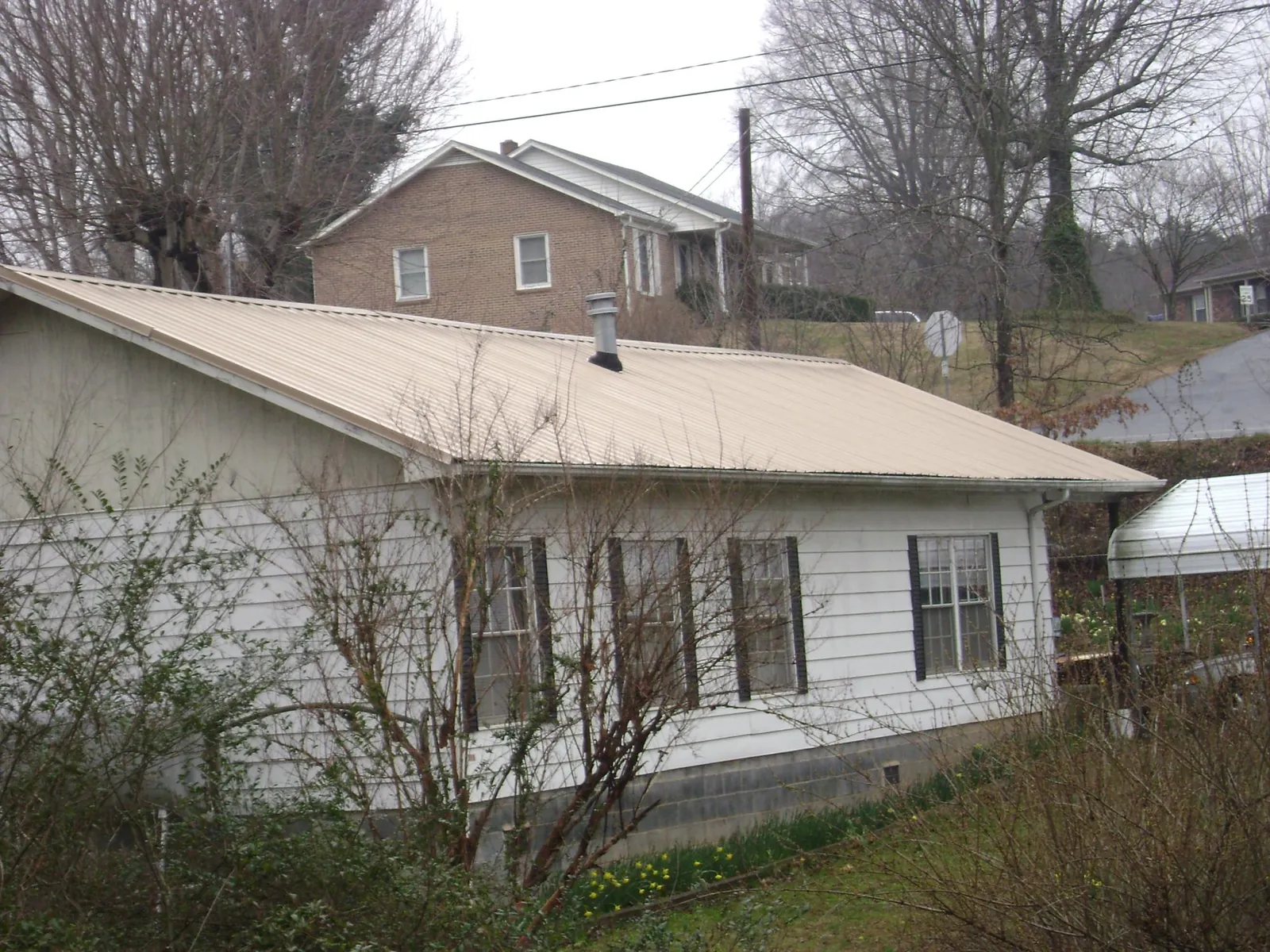 Tan metal roof on a white sided house set into a hillside — Commercial Roofing by Roofing Brothers in West College Corner